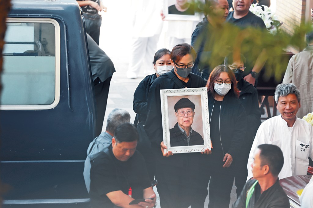 身為家中唯一男丁的馬國明負責捧父親遺照，神情哀傷。