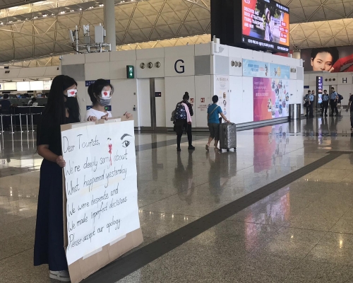 兩名右眼貼染紅紗布的示威者在禁區外向旅客說對不起。