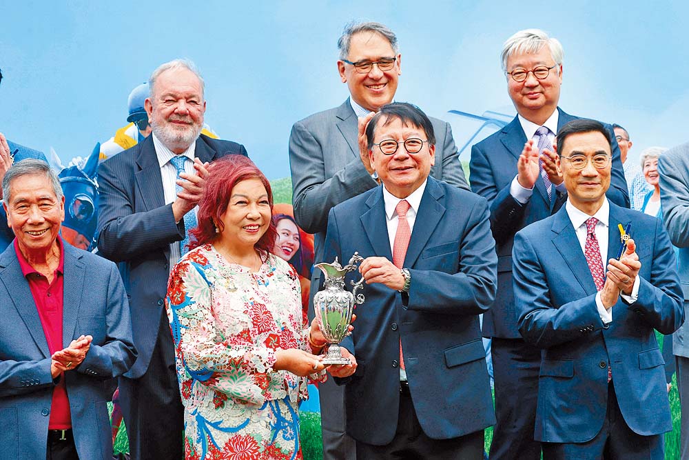 香港特別行政區政府政務司司長陳國基（前排右二）於「香港賽馬會社群盃」賽事後，頒發獎盃予頭馬萬事快的馬主伍燕梅（前排左二）。賽事頒發的獎盃已有超過170年歷史，由收藏家雷剛先生捐贈，以表揚馬會對社會的貢獻。