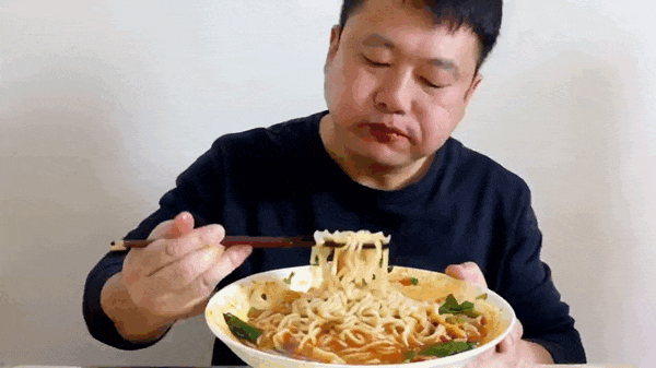 提示词：一个中国男人坐在桌前，用筷子吃面条。