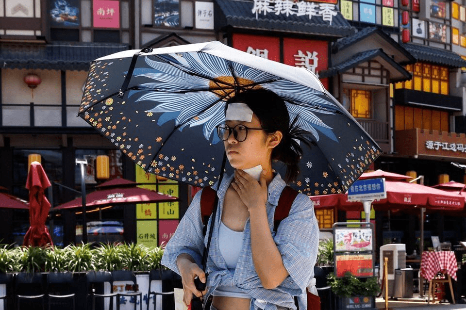 北京女子撐陽傘走在路上。路透社