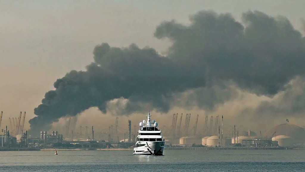 伊朗對杜拜發動攻擊，一艘遊艇駛經傑貝阿里港（中東最繁忙港口）升起的濃煙。