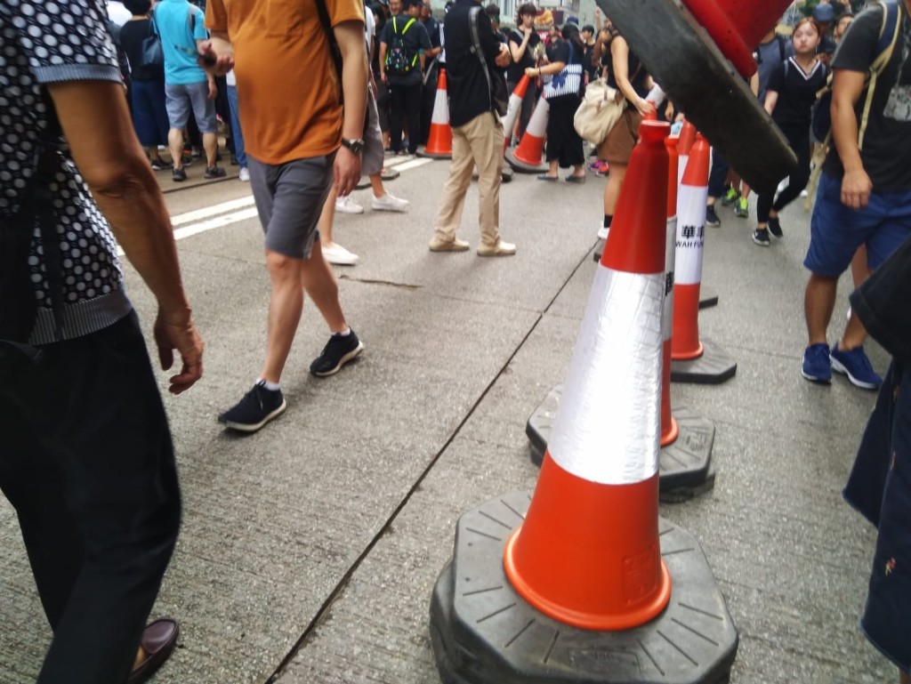 由於相反方向的遊行重疊,有市民將置於電車路旁的雪糕筒移開開路。