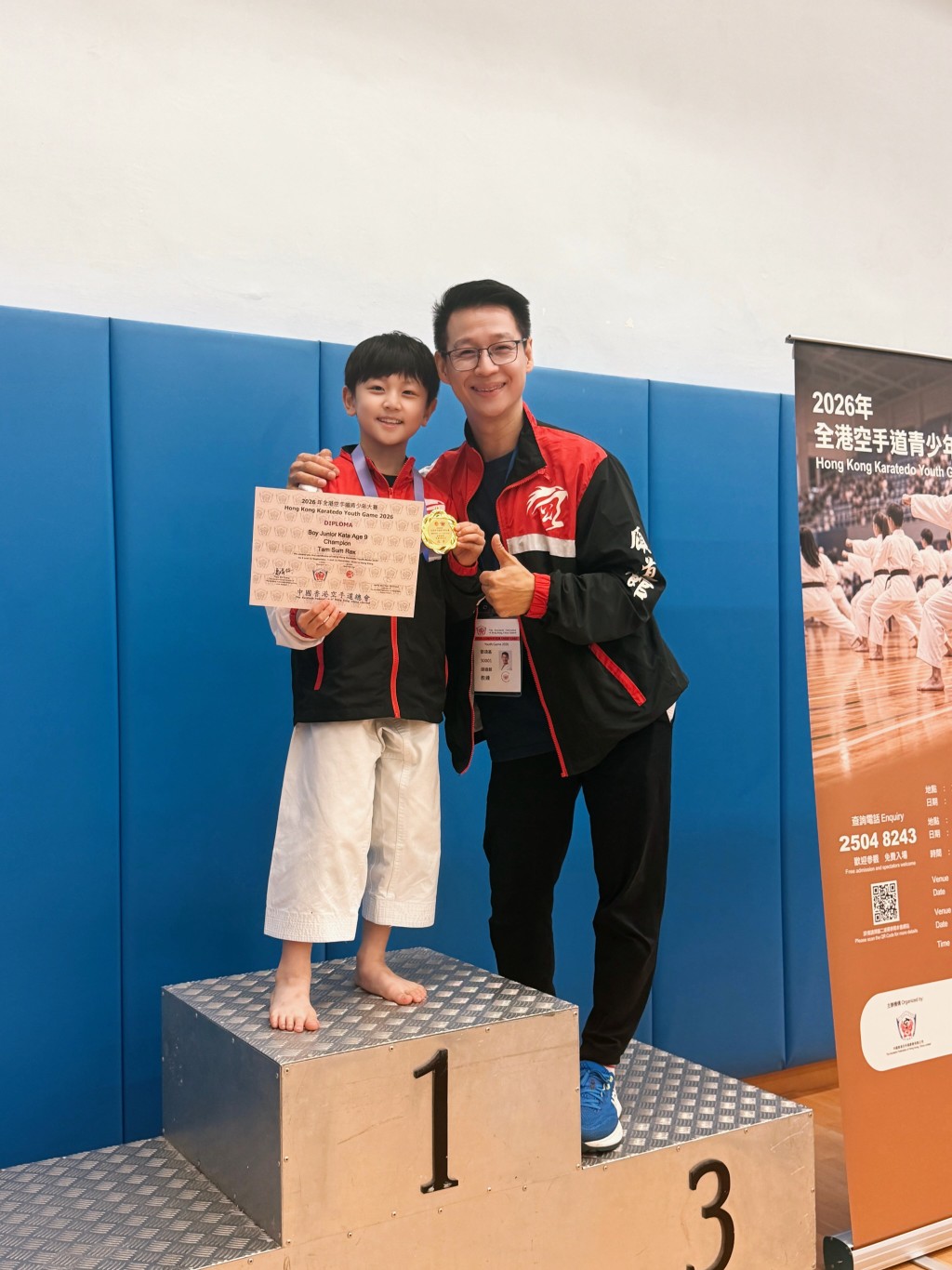 譚俊彥9歲兒子譚杺勇奪全港空手道比賽金牌，站在冠軍領獎台後，與教練開心合照留念。