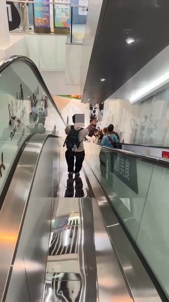 男子翻越玻璃欄杆,爬落扶手電梯中間的銀色蓋板,之後沿著蓋板慢慢爬行到下一層。Threads@showerrrjun片段截圖 男子翻越玻璃欄杆,爬落扶手電梯中間的銀色蓋板,之後沿著蓋板慢慢爬行到下一層。Threads@showerrrjun片段截圖
