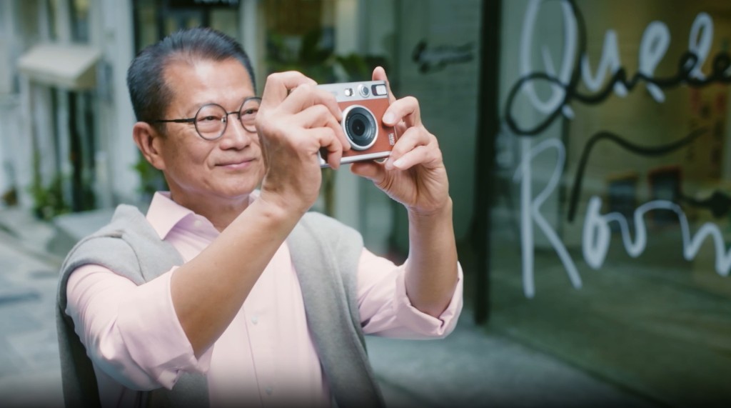 陳茂波手持相機遊走各大街小巷。財政預算案專頁影片截圖 陳茂波手持相機遊走各大街小巷。財政預算案專頁影片截圖