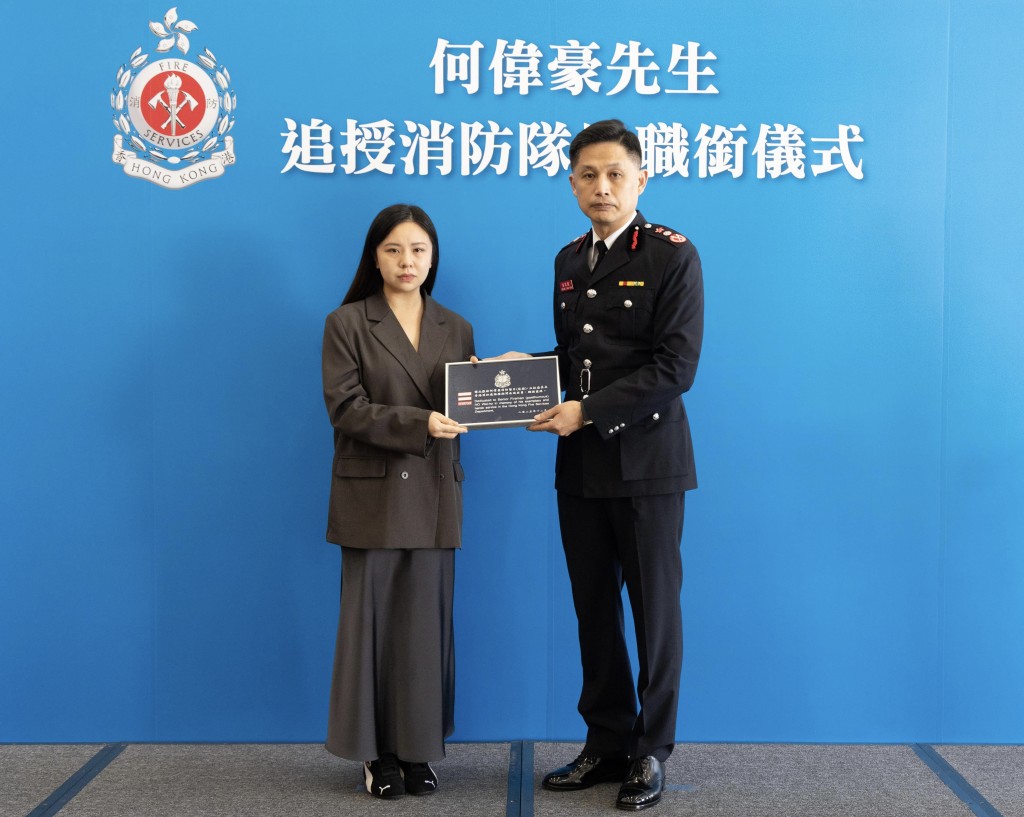 消防處處長楊恩健（右）頒授消防隊目階級章刺繡，由何偉豪家人代表接受。