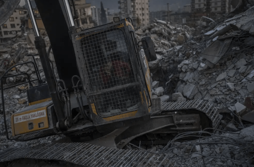 2 月 12 日，星期日，一名挖掘機司機正在等待救援隊從土耳其東南部安塔基亞一座倒塌的建築物中救出一名地震遇難者的屍體。AP