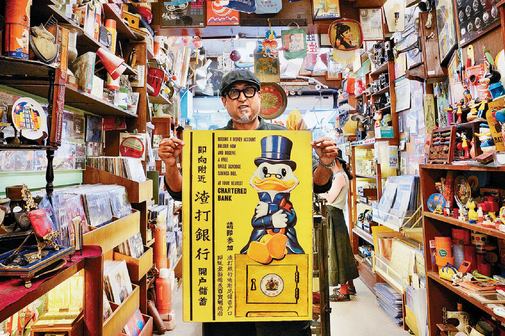 ■经营怀旧物品店的Mido，展示印有迪士尼卡通图案的银行开户广告。