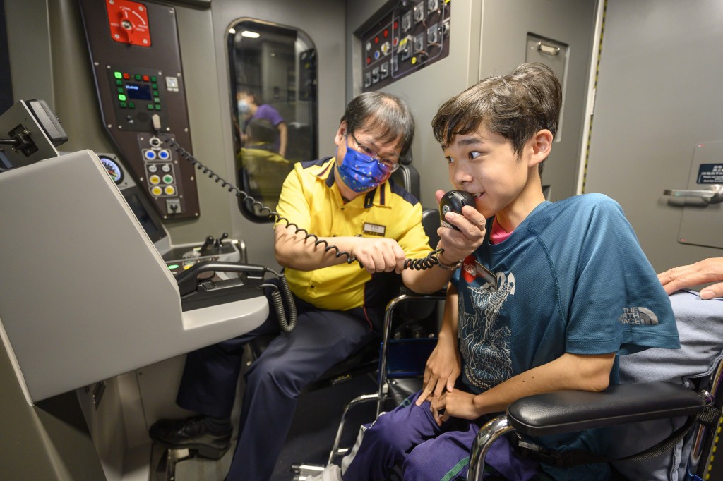 列车员工主任黄锦昌(左)向梓键递上对讲机， 让梓键作车长广播。