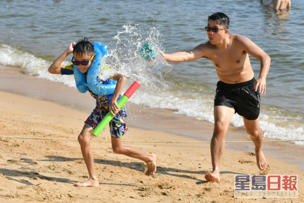家长与小朋友在沙滩玩水消暑。
