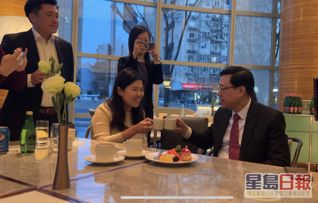 李家超（右1）与一众记者尝试北京传统饮品豆汁，特首办传讯秘书谢振中（左1）亦有出席。