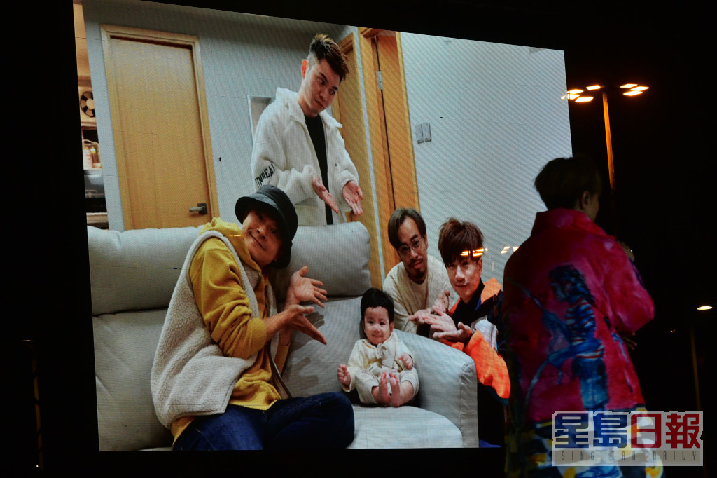 銀幕上播放出四子圍着一個嬰兒的照片。