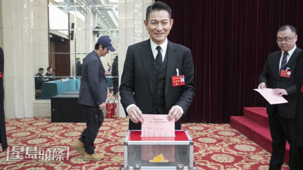 刘德华投票时脸露笑容，背后“路过”的戴帽男子，正是吴京。（《星岛》图片）