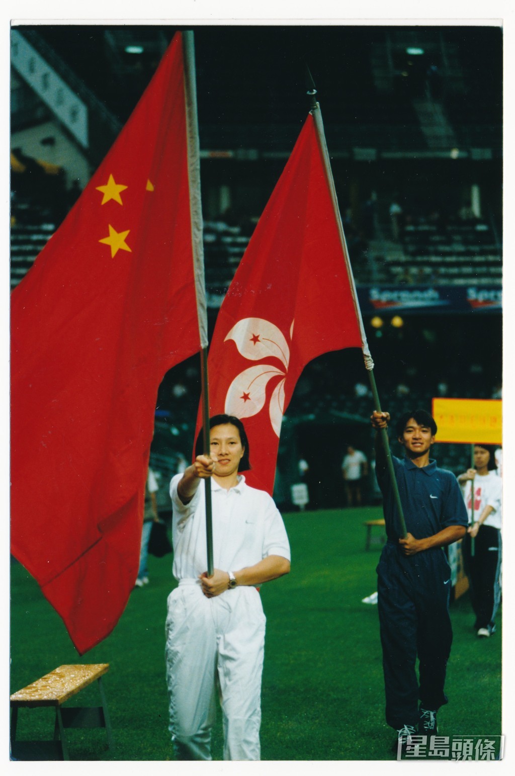 1997年7月李丽珊及自行车手黄金宝手持中国国旗及特区区旗，在大球场回归杯赛前引领56支体运队伍健儿，绕场一周。