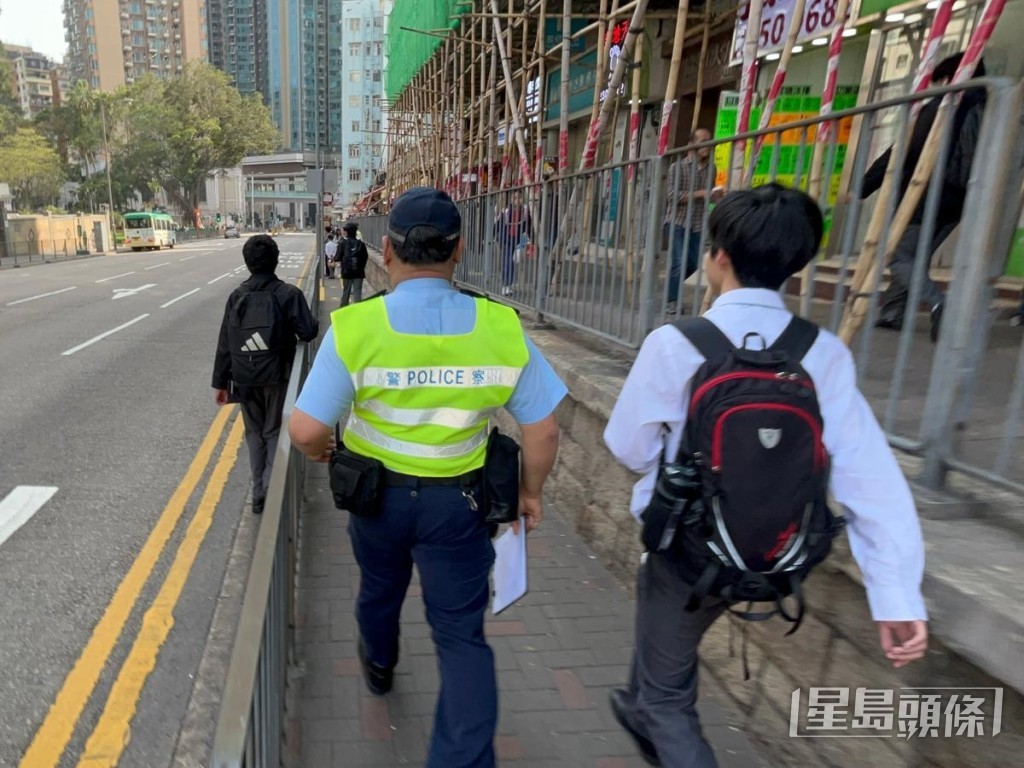 中学生于行人路栏杆外边缘行走,被警员警告。 中学生于行人路栏杆外边缘行走,被警员警告。