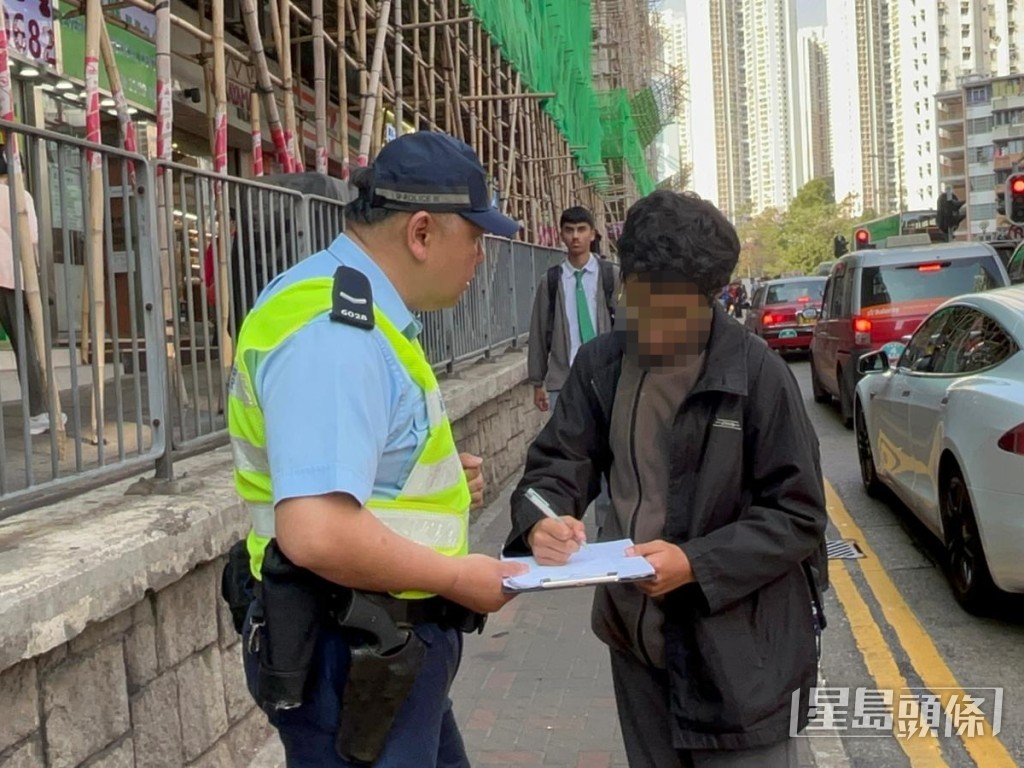 中学生于行人路栏杆外边缘行走,被警员警告。 中学生于行人路栏杆外边缘行走,被警员警告。