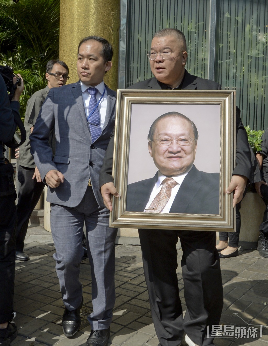 金庸兒子查傳倜（右）手捧父親遺像登上靈車。