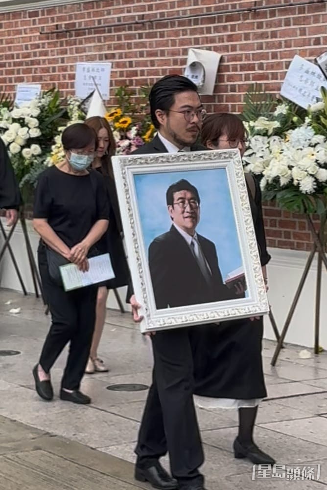 長子李啟旻醫生神情哀傷捧住父親遺照，而胞弟阿Mo李啟言因在在醫院未能親自送別爸爸。