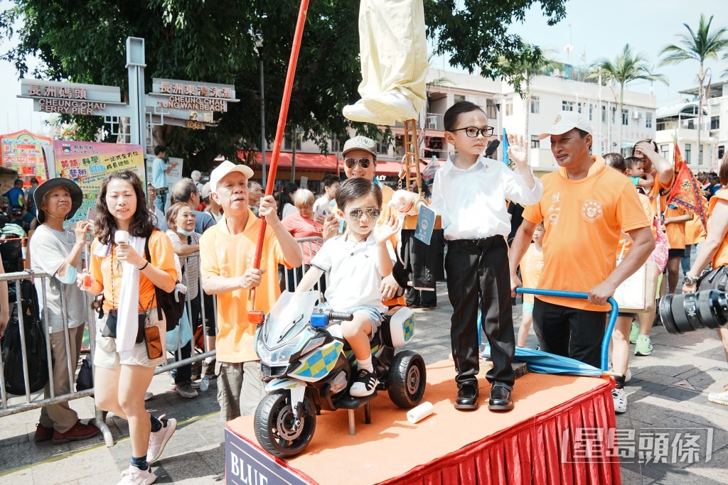 有小孩扮成車手。後方的小孩相信是扮演保安局局長鄧炳強,讚揚其帶領的保安局團隊,齊心拯救被扣押在緬甸詐騙園區的港人。 有小孩扮成車手。後方的小孩相信是扮演保安局局長鄧炳強,讚揚其帶領的保安局團隊,齊心拯救被扣押在緬甸詐騙園區的港人。