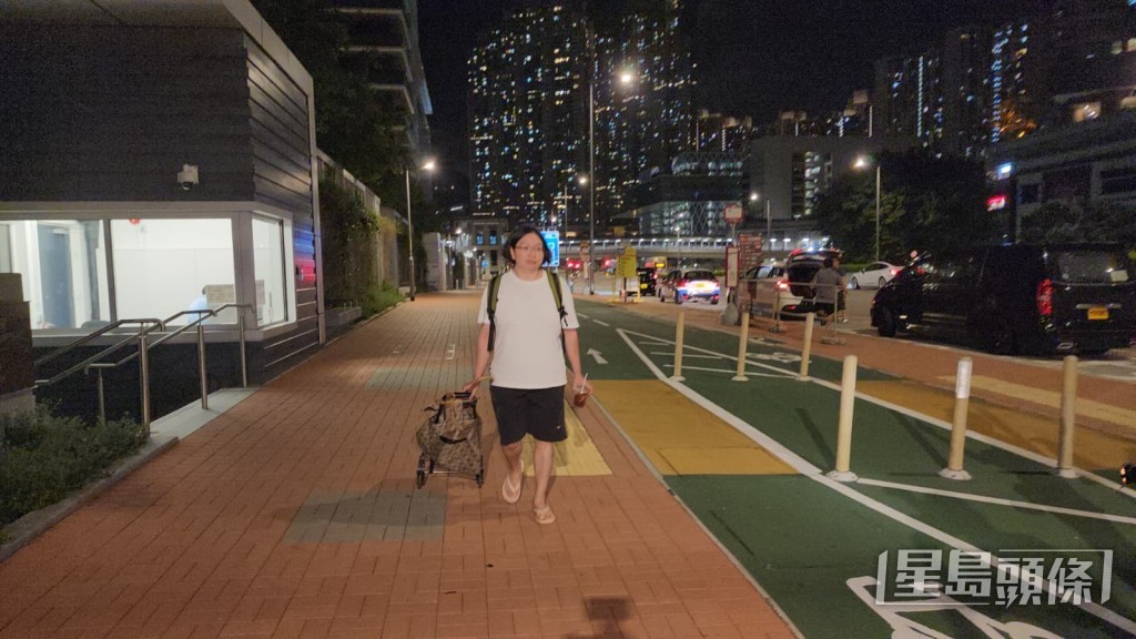 關女身穿白色T恤及黑色短褲,背上背囊並拖着手拉車,手持飲品步出大樓。黎志偉攝 關女身穿白色T恤及黑色短褲,背上背囊並拖着手拉車,手持飲品步出大樓。黎志偉攝