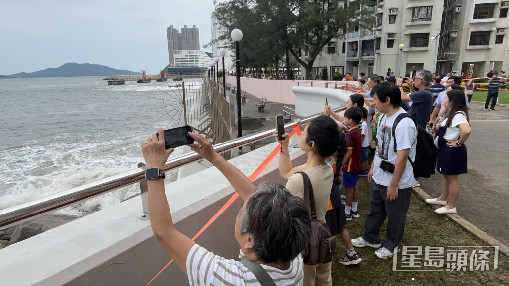 市民在圍牆後觀浪拍照，氣氛熱鬧。