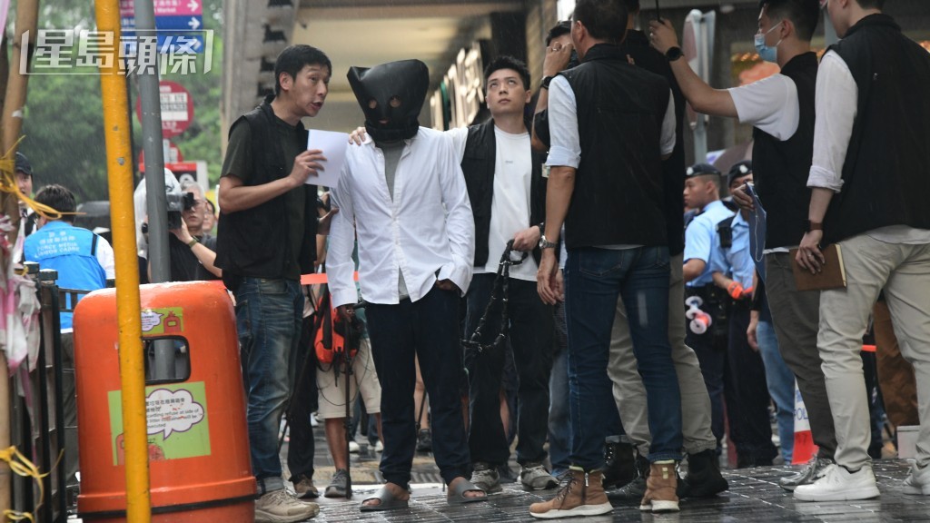 被告巫泰峯(白衣蒙頭)被捕後被帶返現場重組案情。資料圖片 被告巫泰峯(白衣蒙頭)被捕後被帶返現場重組案情。資料圖片