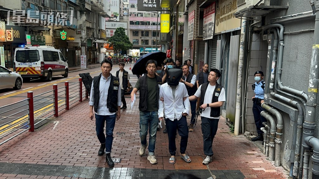 被告巫泰峯(白衣蒙頭)被捕後被帶返現場重組案情。資料圖片 被告巫泰峯(白衣蒙頭)被捕後被帶返現場重組案情。資料圖片