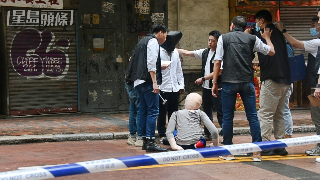 被告巫泰峯(白衣蒙頭)被捕後被帶返現場重組案情。資料圖片 被告巫泰峯(白衣蒙頭)被捕後被帶返現場重組案情。資料圖片