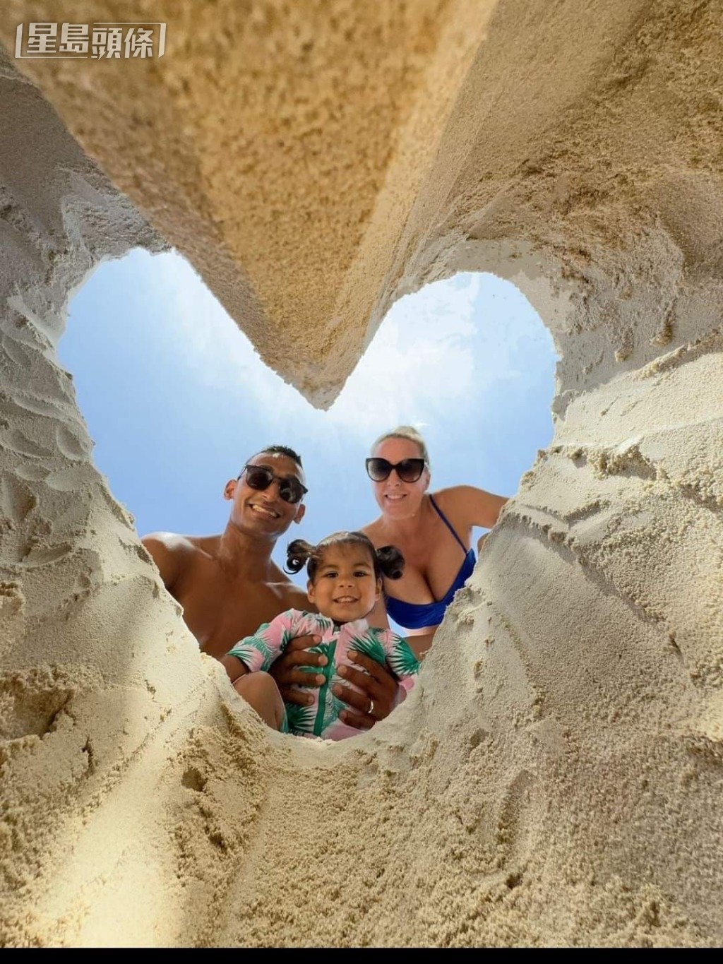 他們一家人在海灘嬉水和玩沙堆時，挖了一個「心」形沙洞，然後把手機放在沙洞底部拍攝，這個另類拍攝一家三口的角度，果然夠特別。