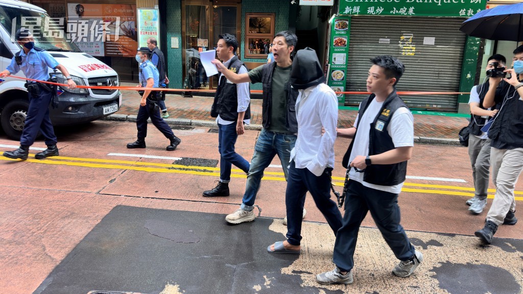 被告巫泰峯(白衣蒙頭)被捕後被帶返現場重組案情。資料圖片 被告巫泰峯(白衣蒙頭)被捕後被帶返現場重組案情。資料圖片
